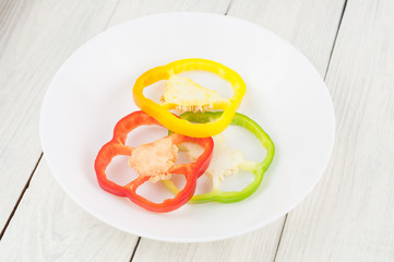 Three slices of colored red and green and yellow fresh ripe raw pepper in ceramic bowl on old rural white wooden planks