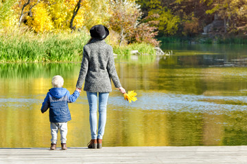 Fototapeta na wymiar Mom and son are standing on the pier by the river. Autumn, sunny. Back view