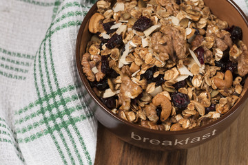 Homemade granola with honey, oatmeal, cashew nut, almond, pistachio, raisin and cranberry in clay bowl,glass with milk on wood dark table,