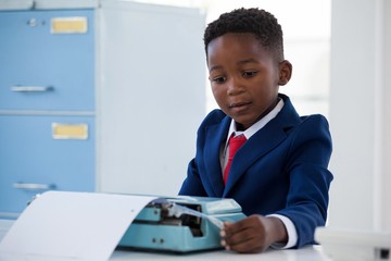 Boy imitating as businessman working on typewriter - obrazy, fototapety, plakaty