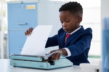 Boy imitating as businessman adjusting paper on typewriter - obrazy, fototapety, plakaty