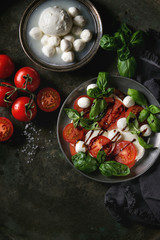 Italian caprese salad with sliced tomatoes, mozzarella cheese, basil, olive oil. Served in vintage metal plate with ingredients above over dark metal background. Top view with space. Rustic style