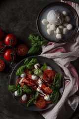 Italian caprese salad with sliced tomatoes, mozzarella cheese, basil in vintage metal plate with ingredients above over dark metal background. Top view with space. Rustic style. Toned image
