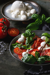 Italian caprese salad with sliced tomatoes, mozzarella cheese, basil, olive oil. Served in vintage metal plate with ingredients above over dark metal background. Close up. Rustic style