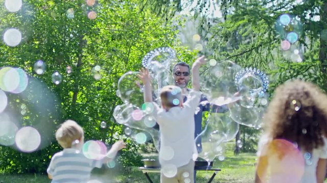 Little boys and girl jumping and catching bubbles in the air while playing at bubble show in park made by professional performer