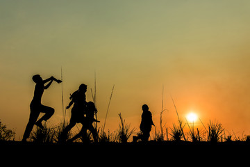 Fototapeta na wymiar Running group of children running on meadow, sunset, silhouette