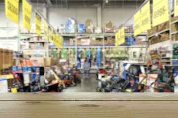 Shop of garden equipment. Lawn mowers. Defocused image. In the foreground is the top of a wooden table or counter.