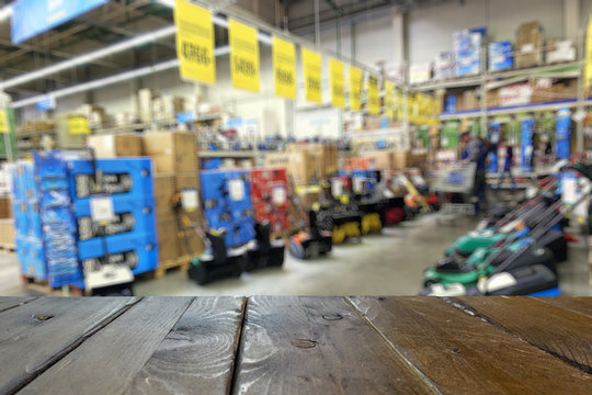 Shop of garden machinery and equipment. Lawn mowers. Defocused image. Wooden table top or counter in the foreground.