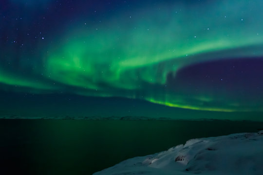Spiral green Northern lights shining over the fjord with mountains in the background, Nuuk, Greenland