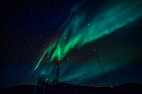 Green waves of Aurora Borealis with shining stars over the mountains and radio tower, Nuuk, Greenland