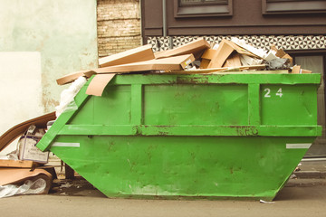 Green garbage container filled with carton boxes