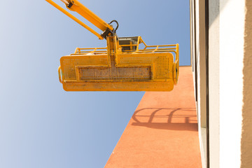 A yellow platform lifted on a hydraulic crane. Painting works. Blue sky on a background.