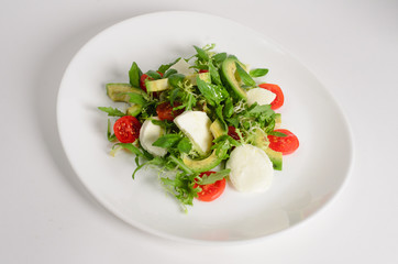 Salad of mozzarella, avocado, cherry tomatoes and arugula in a plate