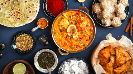 Indian cuisine on diwali holiday: tikka masala, samosa, patties and sweets with mint chutney and spices. Banner coimposition. Dark blue background