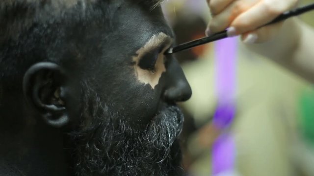 Makeup with black ink for shooting of a bearded man. Backstage