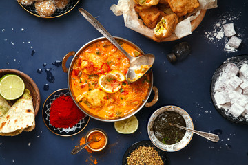 Indian cuisine on diwali holiday: tikka masala, samosa, patties and sweets with mint chutney and spices. Dark blue background