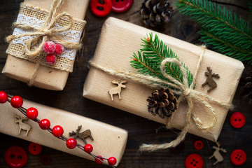 Christmas presents wrapped in kraft paper and tied with burlap twine decorated with red buttons, reindeer, fir branches and pine cones. Overhead view