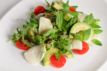 Salad of mozzarella, avocado, cherry tomatoes and arugula in a plate