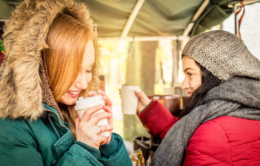 Happy girlfriends best friends sharing time together with coffee takeaway cup in autumn season - Women friendship concept with joyful girls having fun on winter clothes - Bright warm vivid filter mood