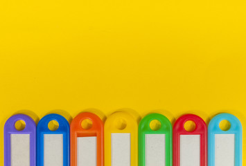 Seven different coloured key holder in a row on yellow background
