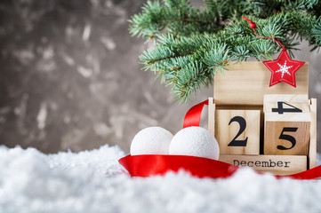 Wooden calendar flipped from 24 to 25 December. Wooden calendar with holiday balls and red ribbon on snow on gray background. Christmas date on calendar. Empty copy space for inscription. Xmas concept