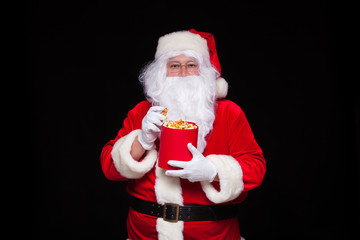 Fototapeta na wymiar Christmas. Photo of Santa Claus gloved hand With a red bucket with popcorn, on a black background