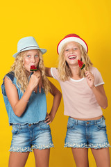 Girls twins holding lollipop and have fun together on yellow background.