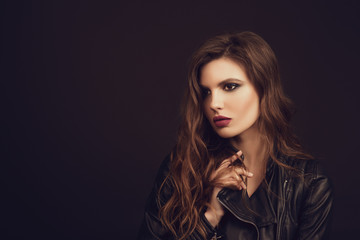 Fototapeta premium Portrait of the beautiful young woman with wavy brown hair posing at studio over black background. Toned.