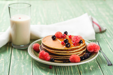 Stack of pancakes with frozen berries poured with honey on wooden kitchen table. Selective focus. Toned.