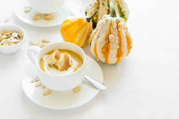 Two cups with fresh pumpkin cream soup decorated cream, seeds and crackers on white table cloth