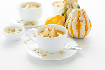 Two cups with fresh pumpkin cream soup decorated cream, seeds and crackers on white table cloth