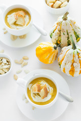 Two cups with fresh pumpkin cream soup decorated cream, seeds and crackers on white table cloth