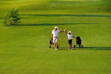 Foto op Plexiglas man met zijn zoon golfers lopen op perfecte golfbaan op zomeravond © alexsokolov