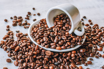 coffee grains scattered over a wooden light surface, porcelain white saucer and a cup.
