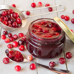   Sweet, healthy dessert. Fresh ripe cranberry and a small glass jar with jam on an old wooden table.