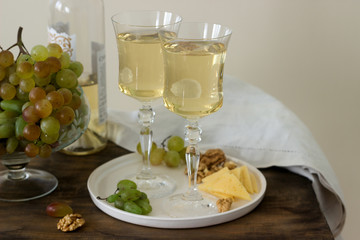 Glasses with white wine and a bottle of wine with a snack - cheese, walnuts and grapes. Rustic style.