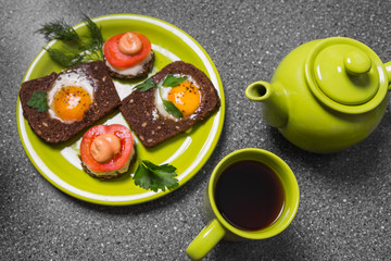 Breakfast -  toast with processed cheese tomato, fried eggs , fried eggs, teapot and cup of tea on a gray  background.