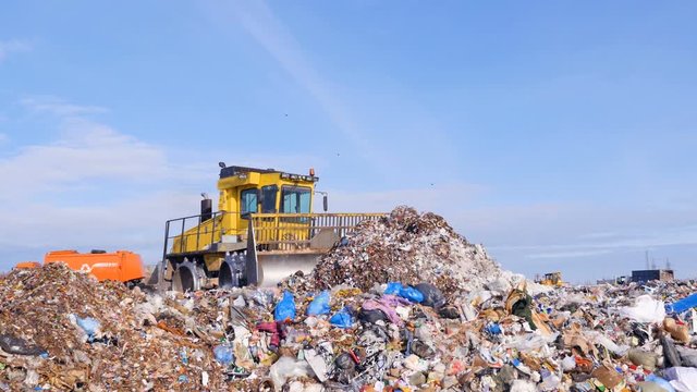 A landfill compactor bulldozer levels down a pile of trash. Water, air contamination concept.