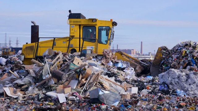 A landfill tractor works among high piles of garbage at landfill. 4K.
