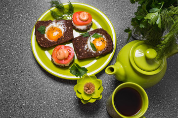 Breakfast -  toast with processed cheese tomato, fried eggs , fried eggs, teapot and cup of tea on a gray  background.