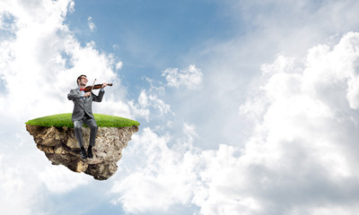 Handsome violinist on floating island in blue sky play his melody