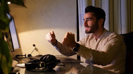 Excited happy attractive young businessman sitting at desk with computer at home with joyful expression