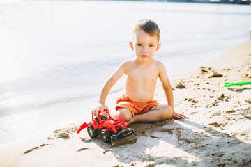 child boy playing on the beach near the river toy red tractor
