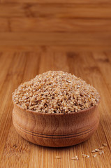 Wheat groats in wooden bowl on brown bamboo board, closeup. Healthy dietary cereals  background.