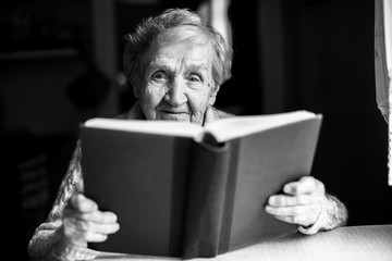 Portrait of an elderly woman reading a book. Black-and-white picture.