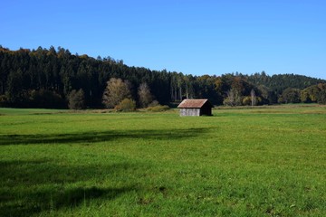 Obraz premium Herbstliche Landschaft mit alter Holzhütte und verfärbten Mischwald in Bayern