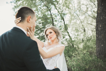 Fototapeta premium Stylish couple of happy newlyweds walking in the park on their wedding day with bouquet