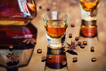 Cognac or liqueur, coffee beans and spices on a glass table.