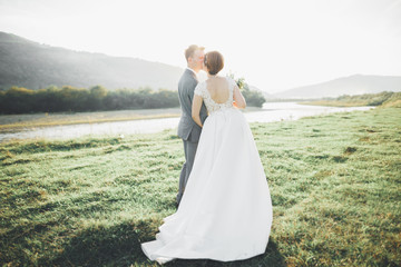 Gorgeous bride and stylish groom walking at sunny landscape, wedding couple, luxury ceremony mountains with amazing view, space for text