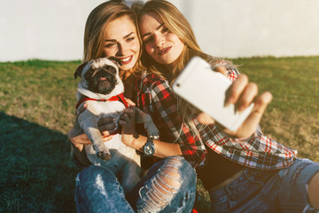 Two beautiful smiling girl sisters twins and dog pug walking in summer park